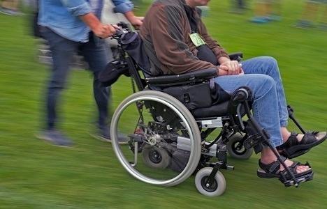 Person i kørestol bliver kørt af anden person på græsplæne
